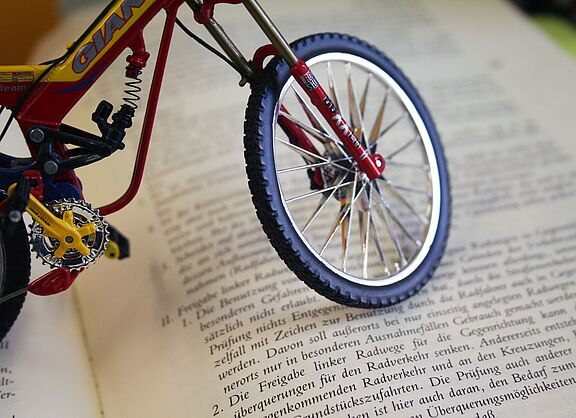 Miniatur-Fahrrad steht auf einem aufgeschlagenen Buch mit deutschem Gesetzestext.